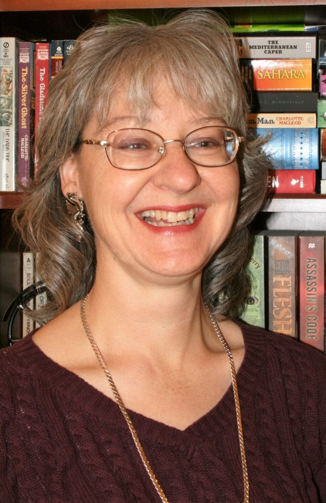 Shari Heinrich, Young Adult Author, stands before her bookcase