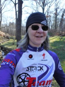 Shari stands in her bicycling jersey before the forest