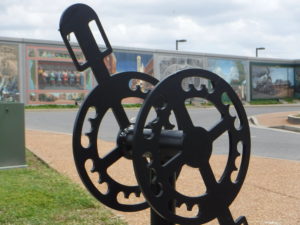 A bike rack shaped like a pedal and gears is the foreground of a floodwall mural